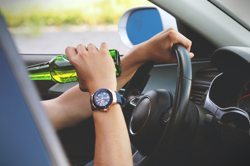 Young Adults Drinking and Driving Close Up of a Persons Arm Holding Up a Green Bottle to Their Mouth While Driving