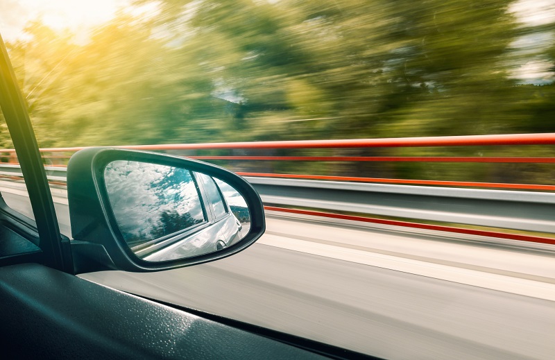 Distracted Driving View of a Side View Mirror on a Car as it Speeds Down a Highway