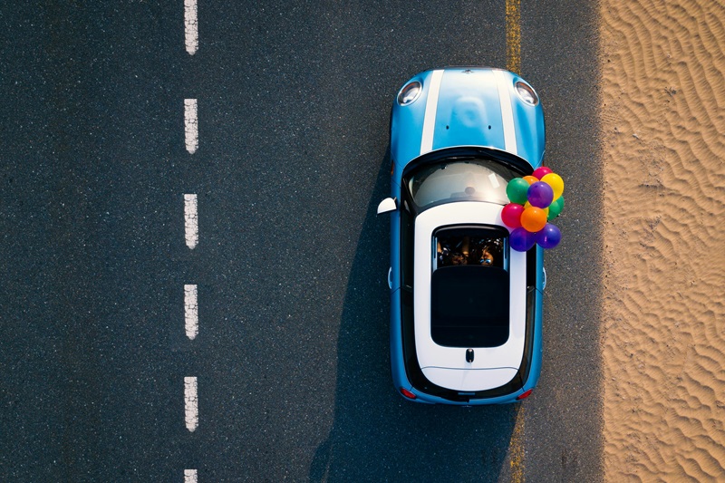 Safe Road Trip Overhead View of a Car Driving Down a Road with Balloons Coming from the Sunroof