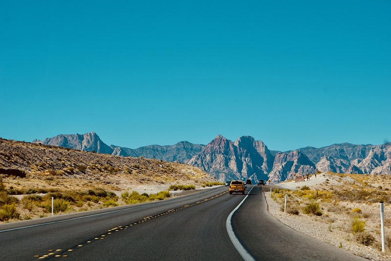 Safe Driving Tips for Summer a Car Driving Down a Road on a Sunny Day with Mountains in Sight