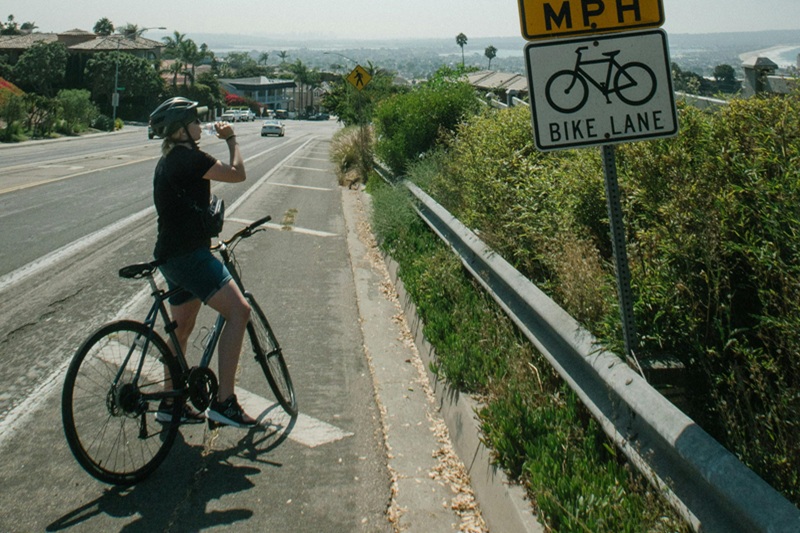 Sharing the Road with Bikers a Woman on a Bicycle Taking a Drink of Water While Resting in a Bike Lane Next to a Sign That Says Bike Lane