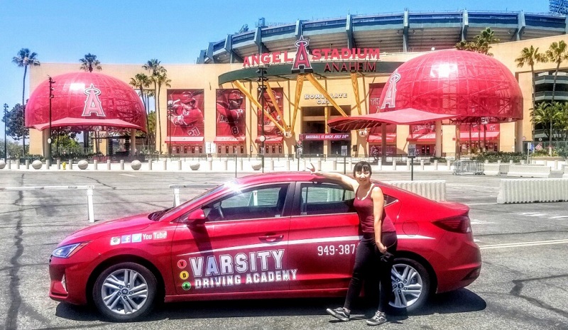 Laguna Drivers Ed a Female Student Standing next to a Training Vehicle in the Angel's Stadium Parking Lot