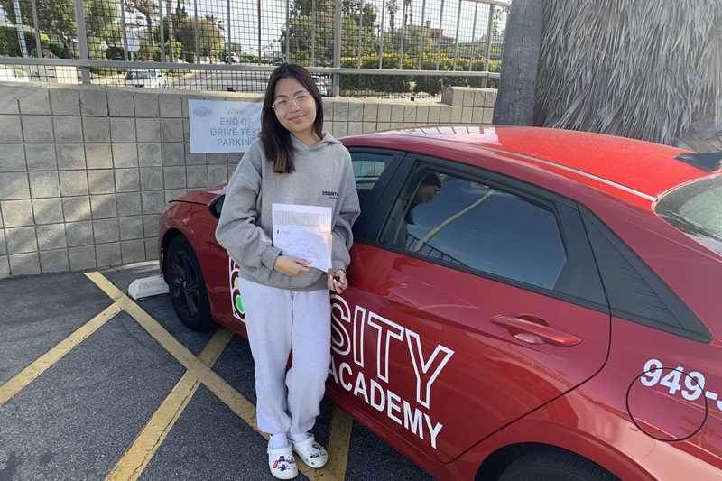 Which Driving School for Woodbridge High School Irvine a Student Standing Next to a Training Vehicle Parked in a DMV Parking Lot