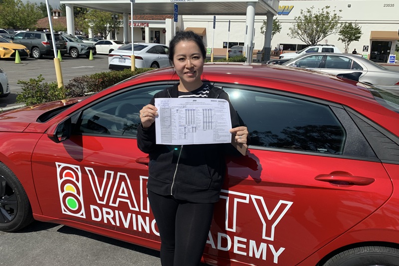 Crean Lutheran High School Driver's Ed Female Student Standing Next to a Training Vehicle Holding Up a Passed Driving Test Sheet