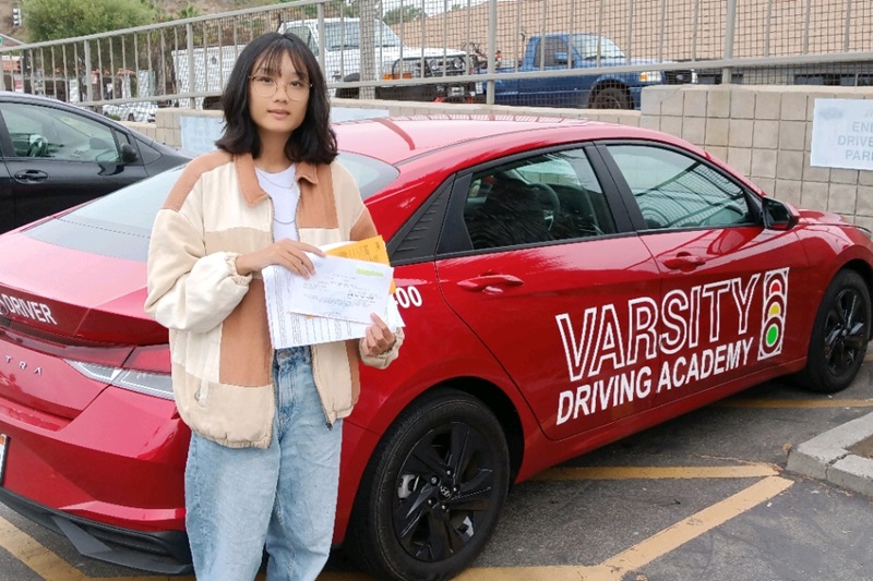 UCI Driver's Ed Student Standing Next to a Training Vehicle in a DMV Parking Lot