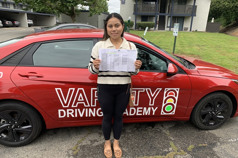 Best Driving School Near Me Irvine Student Standing Next to a Training Vehicle in a DMV Parking Lot